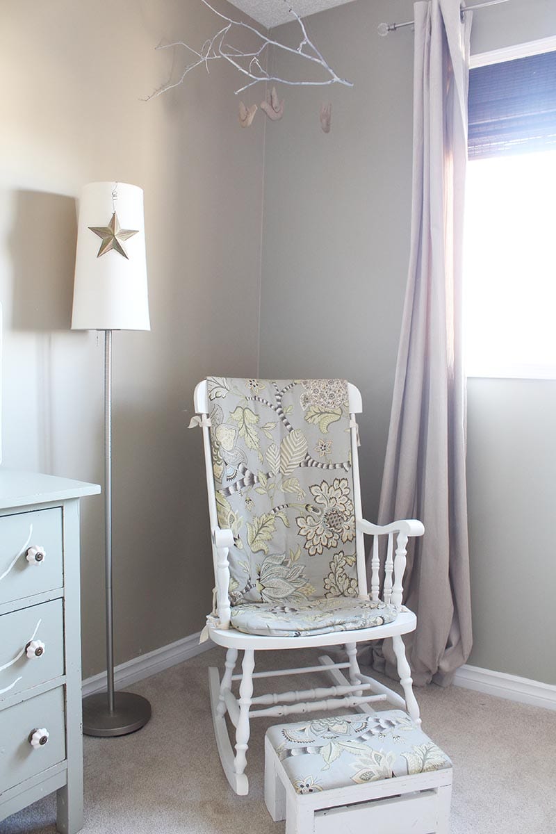 DIY tree branch mobile in a green and beige baby bedroom.