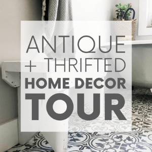 A white and light grey bathroom with an antique clawfoot tub with the words "antique + thrifted home decor tour." Click to visit post.