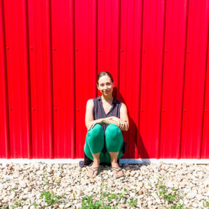 Larissa sitting outside against a bright red wall.