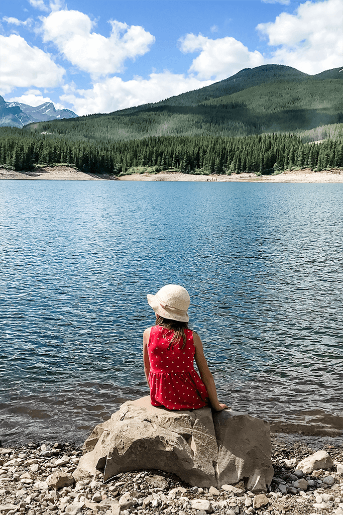 A little girl sitting by a mountain lake.