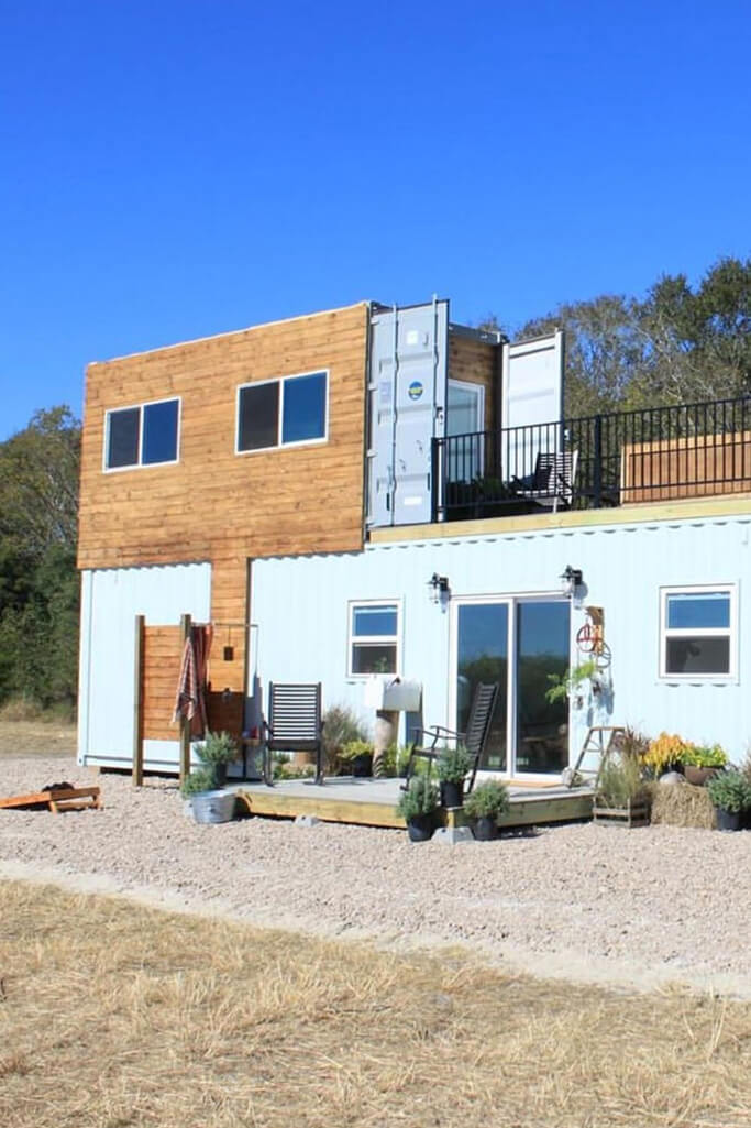 A two-storey shipping container home with white and wood siding.