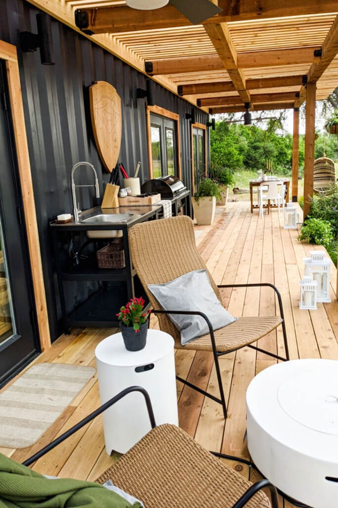 A black container home with a covered wood patio.