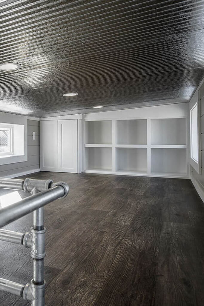 A loft space in a container home with white built-in shelving.