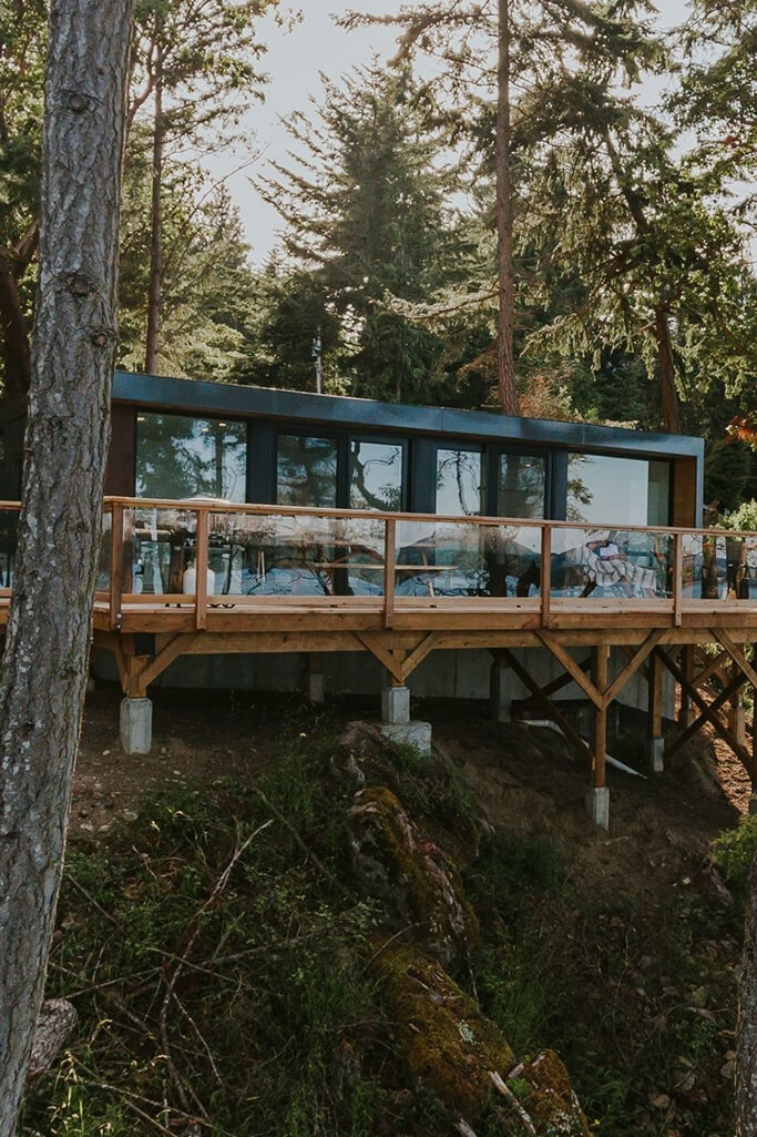 A shipping container home with a wood desk on a hill in a dense forest.