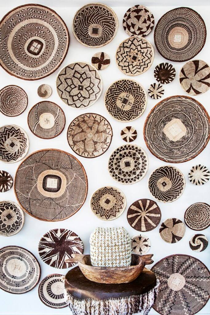 Many brown and beige patterned baskets on a white wall.