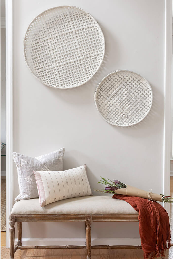Two white baskets hanging on a white wall in front of a bench.