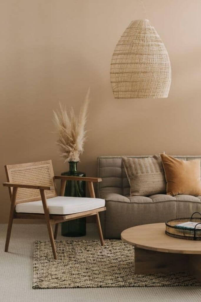 A Japandi sitting area with a dark grey-brown couch, a wooden chair and a woven pendant light.