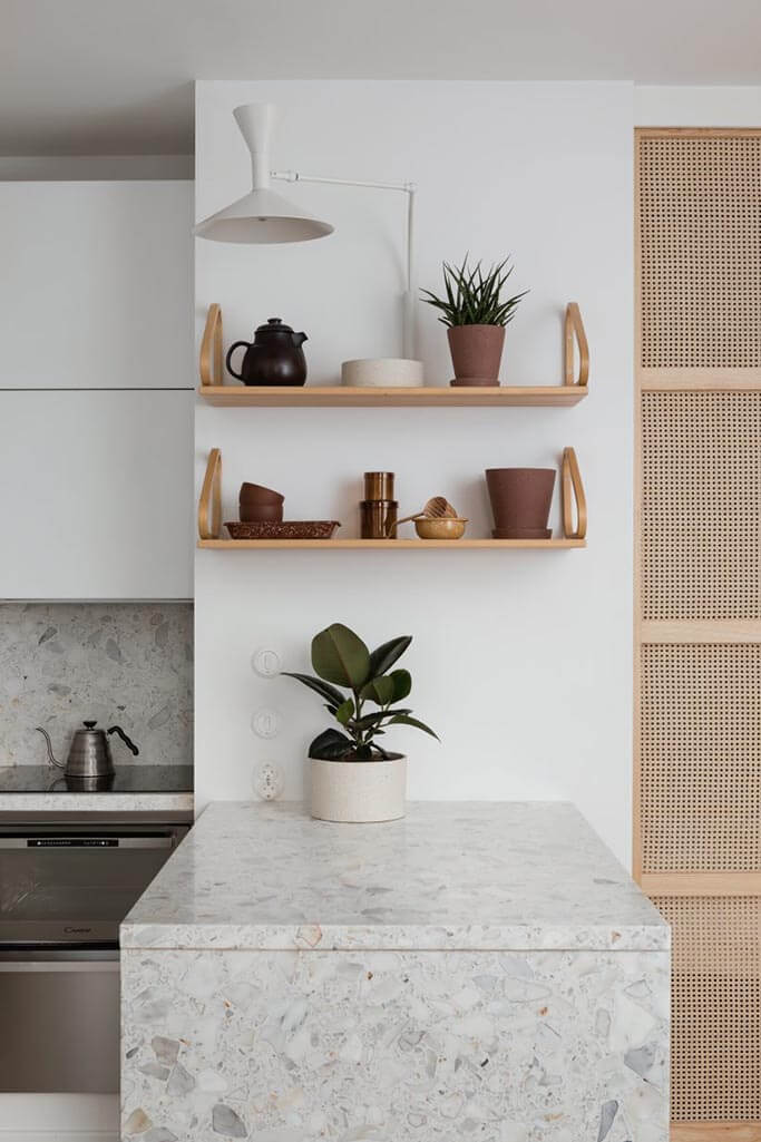 A neutral kitchen with a light grey counter and wooden shelves.