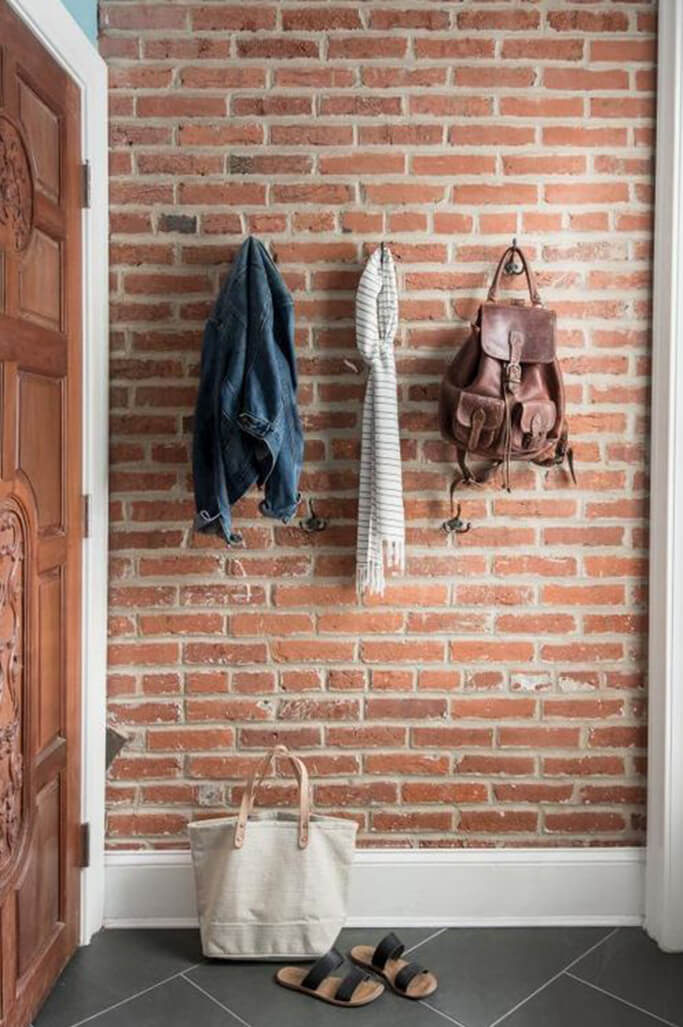 A red brick wall with a jacket, sweater and bag hanging on it.