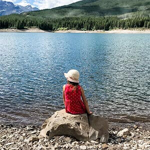 A little girl sitting by a mountain lake.