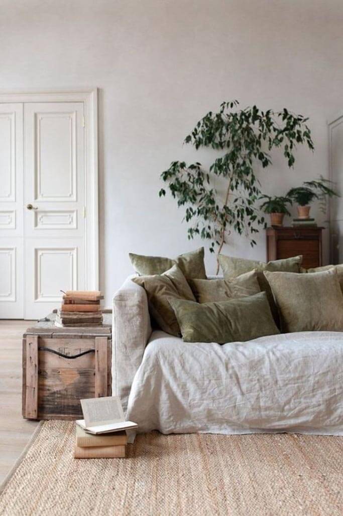 A white couch with green pillows and a rustic chest next to it.