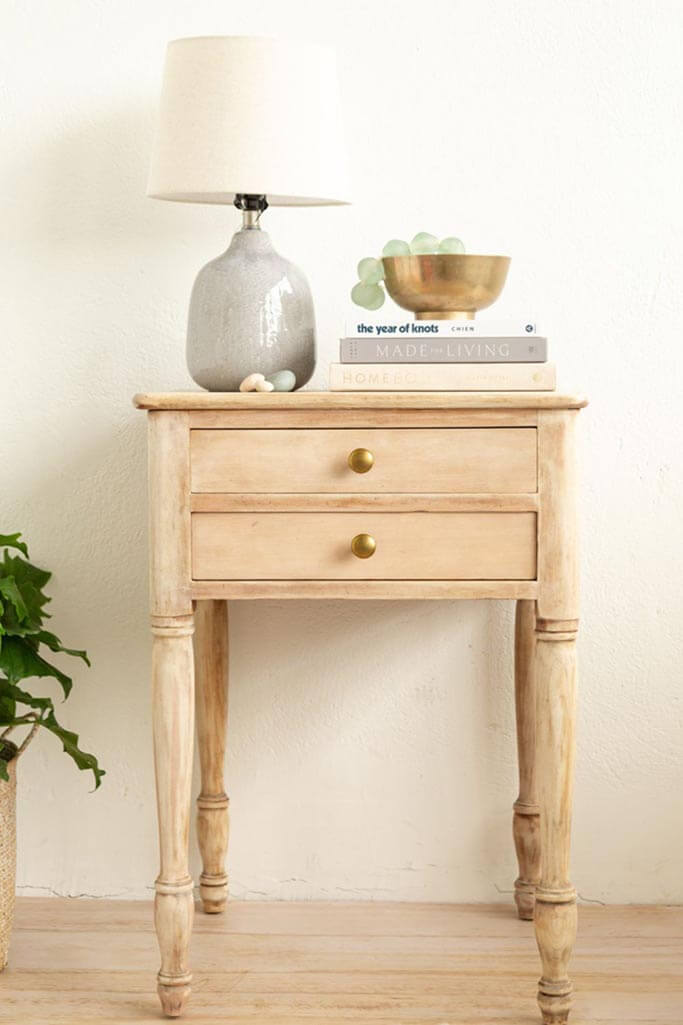 A light wood side table with a lamp and a stack of books on top.