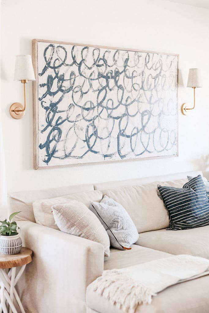 An abstract painting with blue swirls hanging above a beige couch.