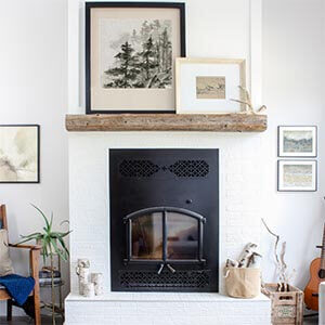 A bright living room with a fireplace and various pieces of neutral coloured art.