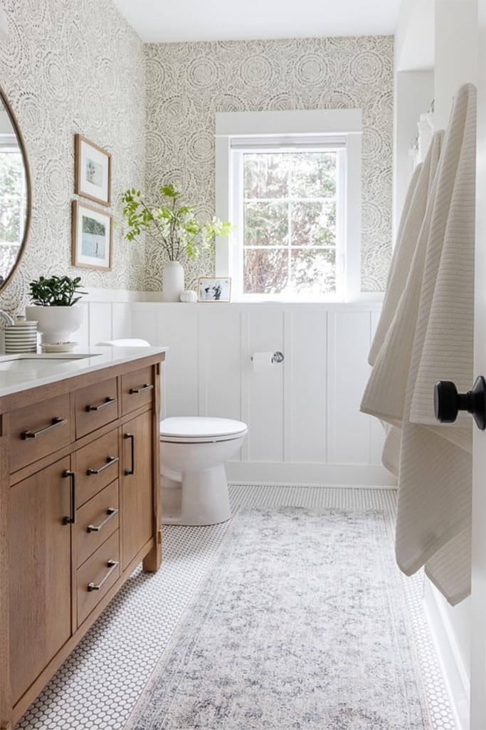A bright bathroom with white panelling and wallpaper.
