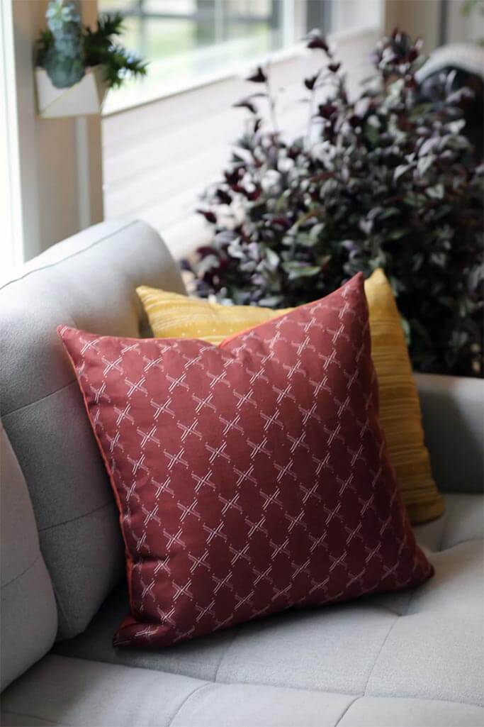 A red and a yellow patterned pillow on a grey couch.