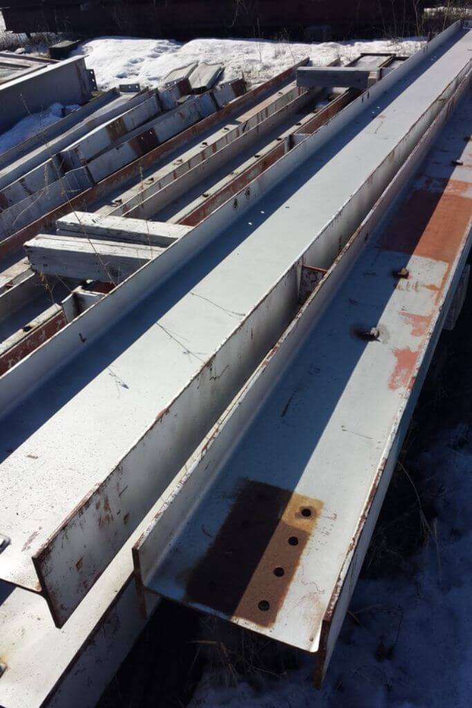 Steel beams sitting in a pile on the ground.
