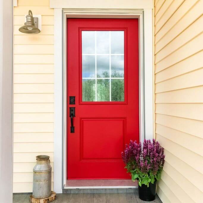 A bright red exterior door on a yellow house.