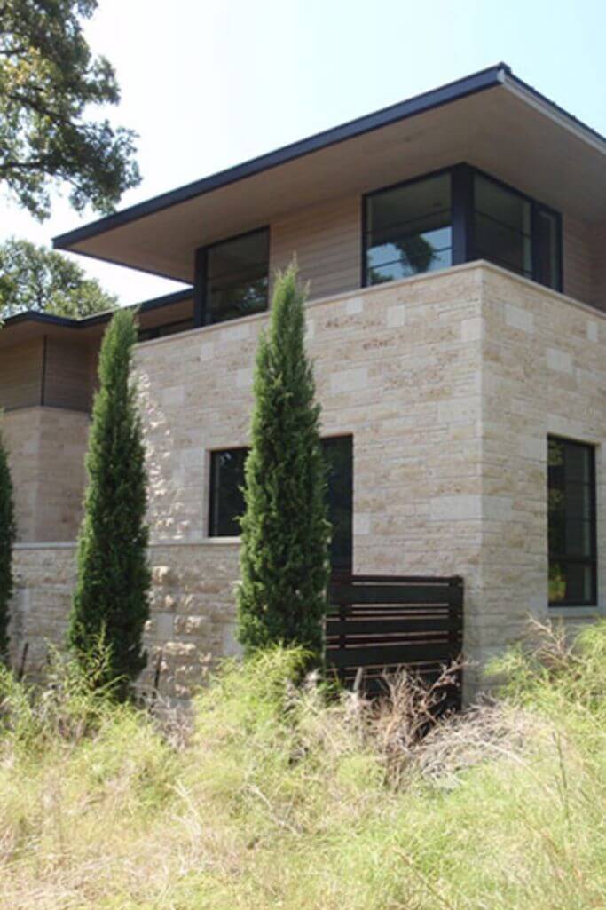 A grey natural stone home surrounded by greenery.
