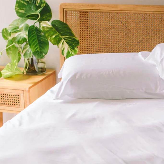 White bedding on a bed with a woven headboard.