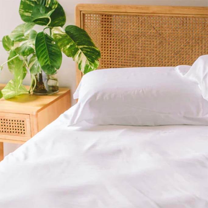White bedding on a bed with a woven headboard.