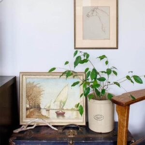An old blue chest with two brass-framed pieces of art and a plant in an old piece of pottery.