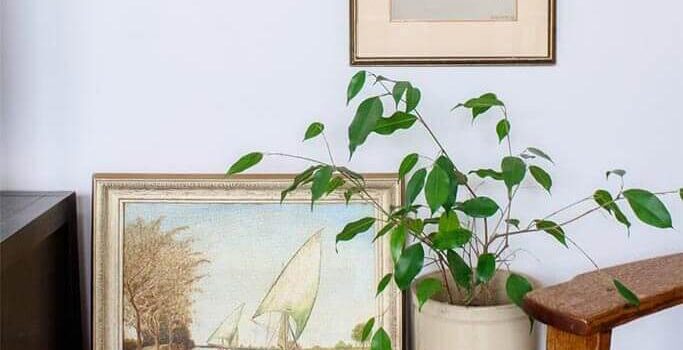 Decorating with Antiques: 5 Tips for Filling Your Home with Unique Vintage Finds An old blue chest with two brass-framed pieces of art and a plant in an old piece of pottery.