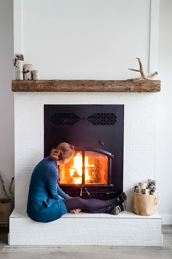 Larissa sitting in front of a fireplace with a fire burning inside.
