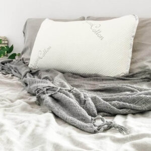 A white pillow sitting on a bed with grey sheets and blankets.
