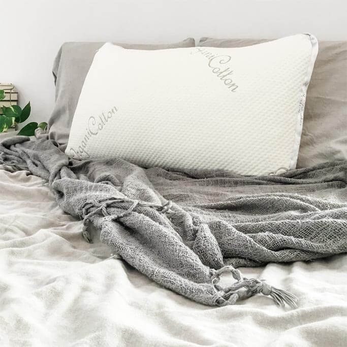 A white pillow sitting on a bed with grey sheets and blankets.