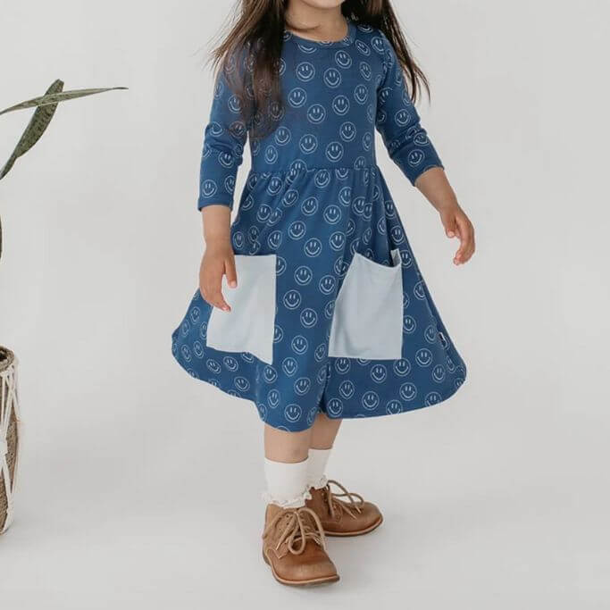 A child wearing a blue dress with smiley faces on it.