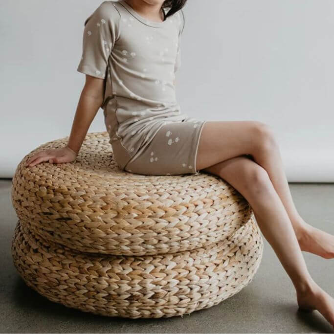 A child wearing a light green pajama set sitting on a woven stool.