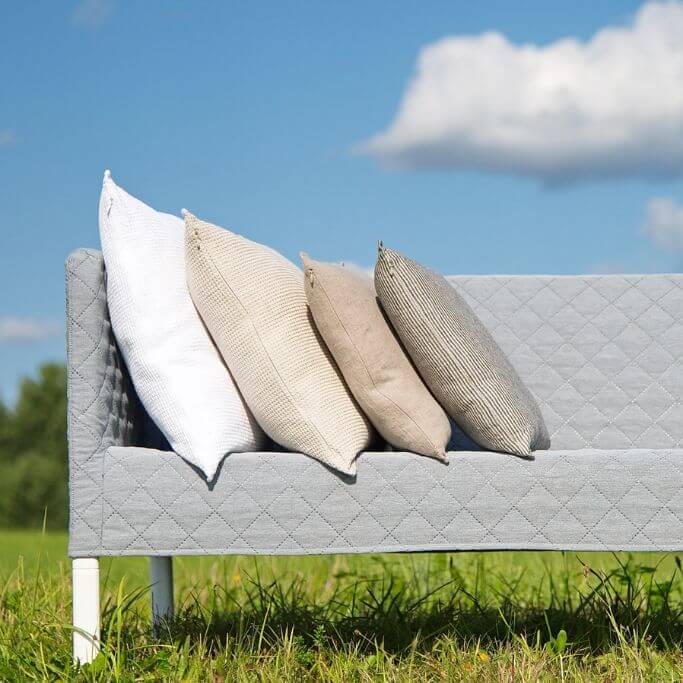 Neutral coloured pillows on grey sofa sitting on the grass.