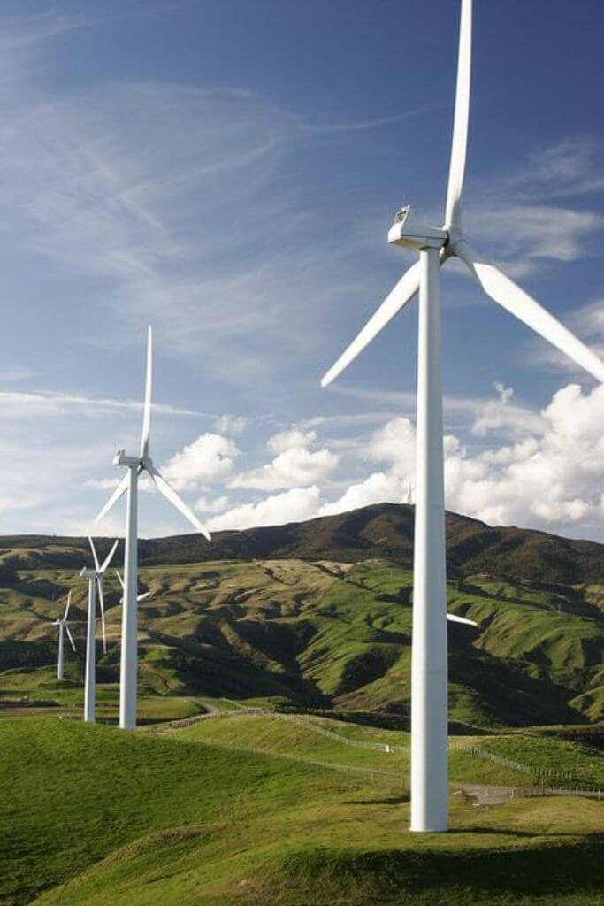 Several large wind turbines on a green hill.