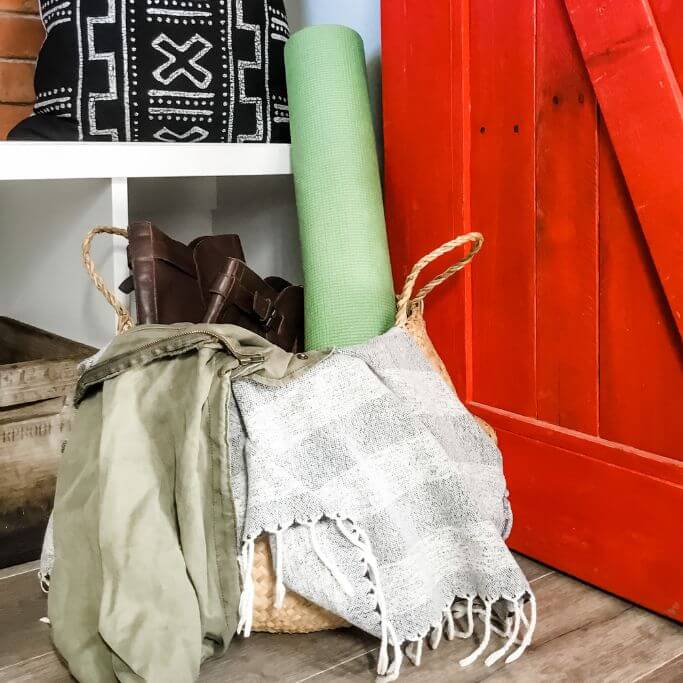 A woven basket filled with odds and ends next to a bright red door.